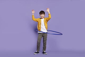 Fototapeta premium Boy exercising with hula hoop on violet background