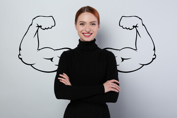 Confident beautiful woman with drawing of strong arms behind her on grey background
