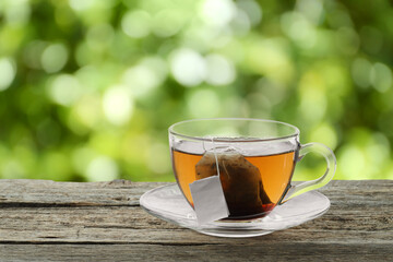 Tea bag in glass cup with hot drink on wooden table outdoors. Space for text