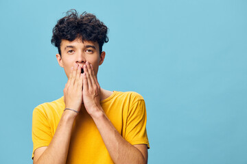 Young man with curly hair showing surprise or shock on a blue background, wearing a yellow t shirt...