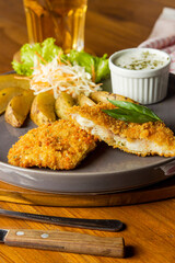 A delicious plate featuring crispy fried chicken, roasted potatoes, fresh salad, and tangy dipping sauce on a rustic wooden table