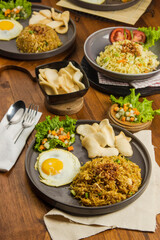Plates of flavorful fried rice accompanied by assorted vegetables, crackers, and a fried egg, presented on a rustic wooden dining table