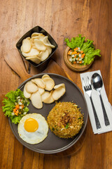 A plate of fried rice topped with a sunny-side up egg, accompanied by fresh salad and crispy chips, beautifully arranged on a rustic wooden table