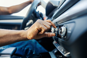 Close up of black car driver's hand changing radio station in a vehicle.
