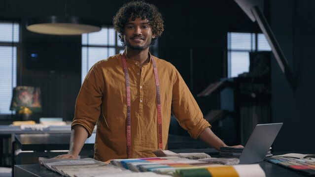 Portrait of happy Indian Arabian man cloth designer at modern tailoring dressmaking studio smiling male tailor couturier in garment workshop small business hand craft fashion fabric clothing design