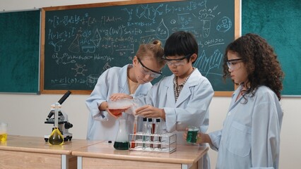 Children doing experiment in science lesson while standing at blackboard at laboratory. Happy student discovering and learning about biochemical liquid while inspecting and mixing sample. Pedagogy.