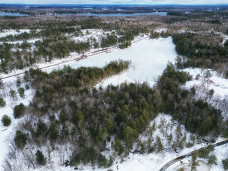 Aerial drone shot over a frozen Spiers Lake towards railroad tracks in rural cottage country Bala, located in the Muskoka Lakes region of Ontario, Canada. Evergreen trees and snow during a cold winter