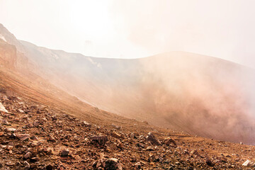 Side view of the crater opening of erupting volcano. Crater with vulcanic gas inside. Clouds and steam in the sky. Daytime vulcanic eruption