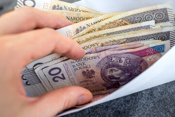 A hand holding an envelope filled with Polish zloty banknotes