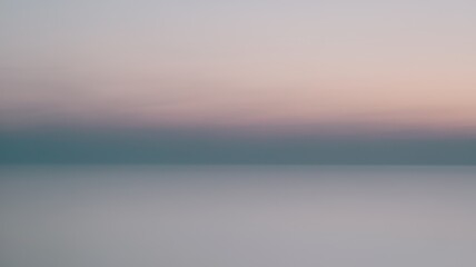 Obraz premium A serene gradient of pastel colors spreads across the horizon, blending hues of soft blue, pink, and lavender over a calm water surface.