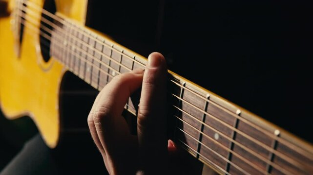 Young musican man checking strings of acoustic guitar close-up. Male guitarist tuning sound of musical instrument. 