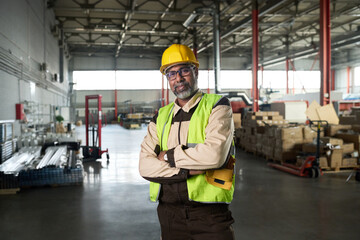 Confident mature male worker of modern factory looking at camera while standing in spacious workshop with packages