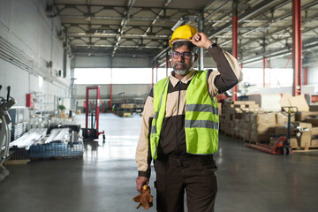 Experienced male worker of factory putting on yellow protective helmet while standing in spacious workshop or plant