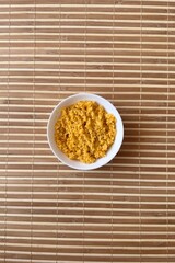 Yellow rice porridge cooked in milk with pumpkin spice in a white bowl on bamboo background. Close-up