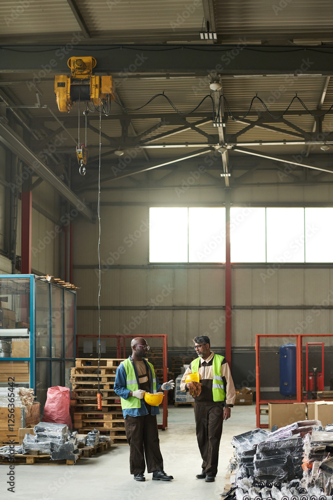 Poster two male workers of modern factory discussing quality of equipment while standing on aisle between s