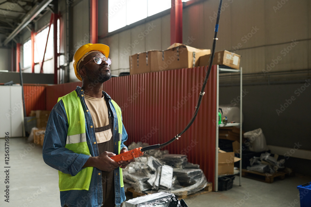 Poster Young African American factory worker looking upwards and pressing buttons on control pad while working in warehouse