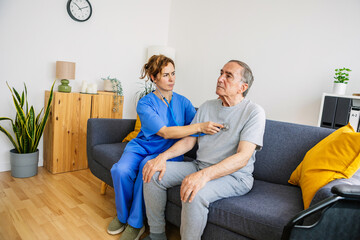 Female nurse examining senior man's chest with stethoscope during home visit, providing healthcare and support for elderly patient