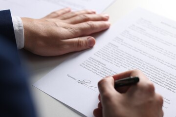 Man putting signature on document at table, closeup