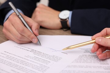 Woman pointing at document and man putting signature at table, closeup