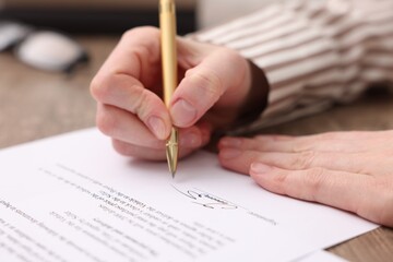 Woman putting signature on document at table, closeup