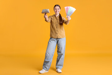 Woman with paintbrush and color selection chart on orange background