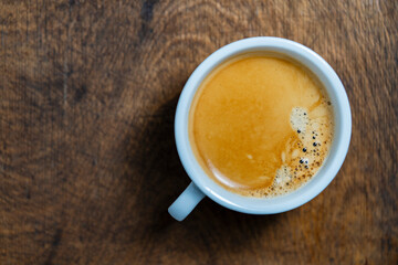 Tasty black coffee in white cup on wooden background, top view, closeup, copy space