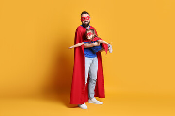 Father and his cute little daughter wearing superhero costumes on orange background