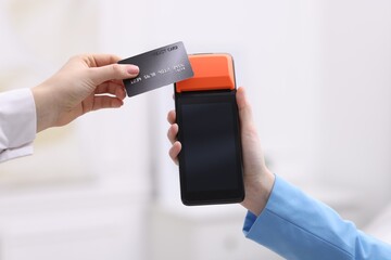 Woman paying with credit card via terminal against blurred background, closeup