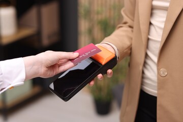 Naklejka premium Woman paying with credit card via terminal against blurred background, closeup