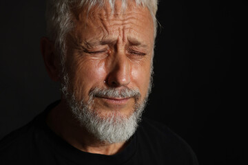 Sad senior man crying on black background, closeup. Space for text