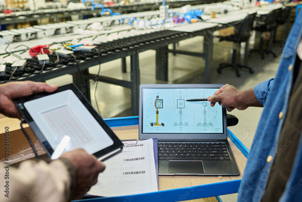 Fototapete hand of male worker of factory pointing at laptop screen with schemes while explaining colleague wit