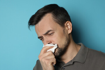 Sad man with paper tissue crying on light blue background