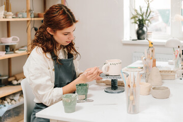 Process of designing cup with a traditional pattern in pottery art studio. Artisan stamps decorative symbols on the dry clay of the cup.