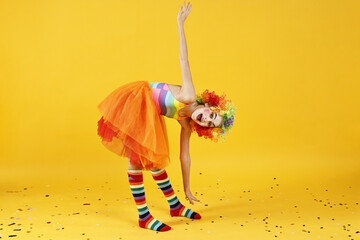 Cute girl dressed like clown and confetti on yellow background. Surprise party
