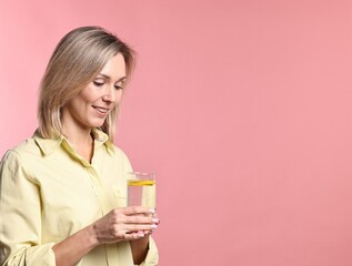 Woman with glass of lemonade on pink background. Refreshing drink