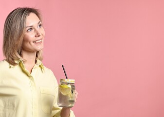 Woman with mason jar of lemonade on pink background. Refreshing drink