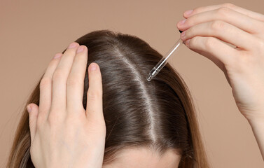 Fototapeta premium Hair loss problem. Girl applying serum onto hairline on dark beige background, closeup