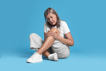 Senior woman suffering from knee pain on light blue background