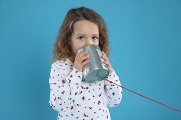 Girl using tin can telephone on blue background