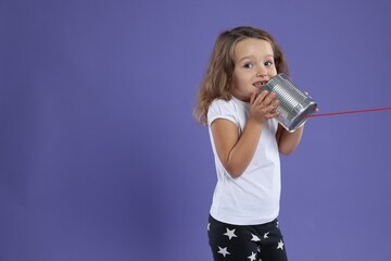 Girl using tin can telephone on violet background. Space for text