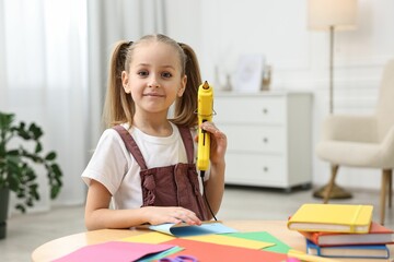 Portrait of little girl with hot glue gun at table indoors