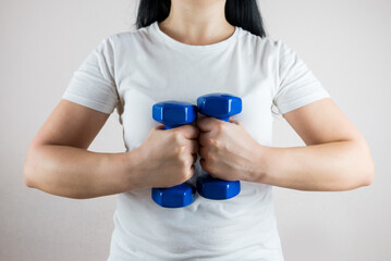 woman in white t-shirt with dumbbells on white. Crop photo, close-up.