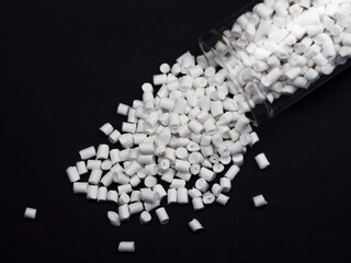 White masterbatch granules spilling from glass tube on black background, polymer carrier of color...