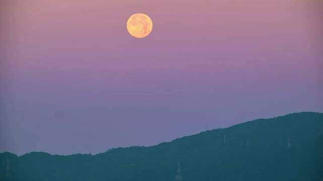 A full moon setting behind the silhouette of XiZhi DaJian Mountain under a pink and orange dawn sky. Spring morning, New Taipei City, Taiwan.