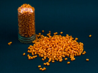 Orange masterbatch granules in glass tube, isolated on black background, color pigment carrier...
