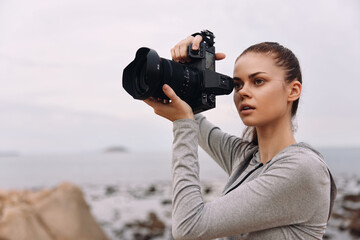 Young woman capturing nature with a camera, wearing a gray sports top and showing focus, with a...