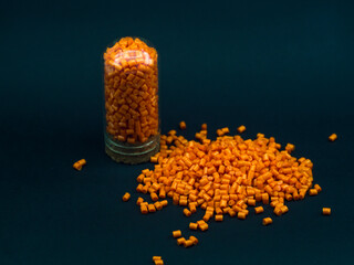 Orange masterbatch granules in glass tube, isolated on black background, color pigment carrier...