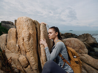 Young woman in outdoor adventure gear resting against a rock by the sea, showcasing determination...
