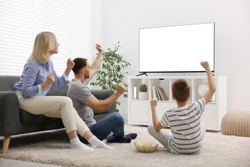 Happy family with snacks cheering while watching tv together at home