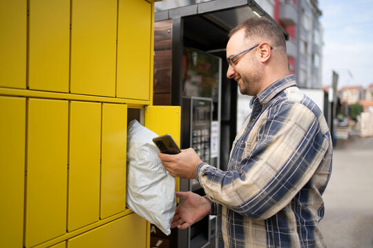 Man using a smart phone to retrieve a package from a yellow delivery locker outdoors